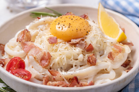Classic carbonara pasta with fried bacon, parmesan cheese and egg yolk. An alternative carbohydrate-free shirataki pasta with carbonara sauce. Large portion in a white plate on a blue background.の写真素材