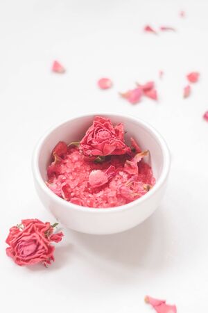 White bowl with sea salt with extract and smell of roses, dried rosebuds on the backgroundの写真素材