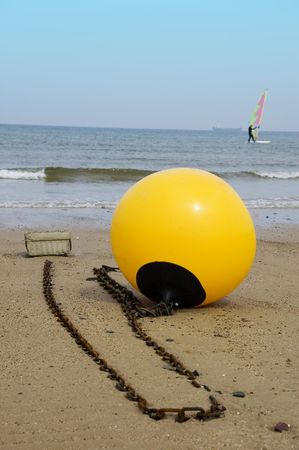 A yellow buoy sits on the beach with a windsurfer &  ship on the distant horizon
の写真素材