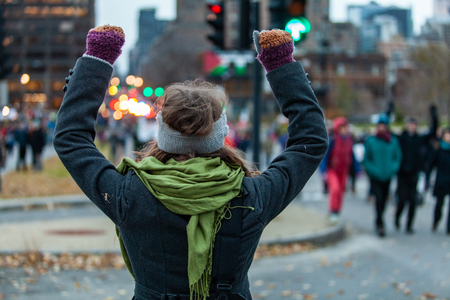 Young woman is raising her arms while at the crowd during an ecological protest. Shot from the backの写真素材