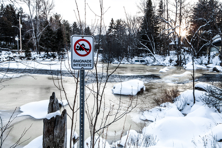 Swimming forbidden sign in front of a partially frozen, fast flowing riverの写真素材