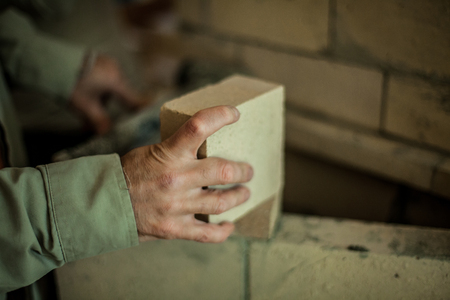 Brickmason's hand holding a brick in front of a brick wallの写真素材