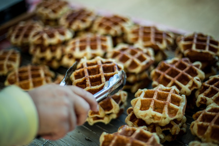 Hand holding a big waffle in kitchen tong, with more waffles in the background, at farmer's marketの写真素材
