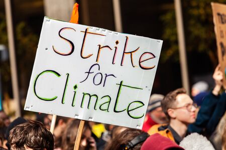 A cardboard placard is seen close-up on a crowded street of environmental activists, saying strike...