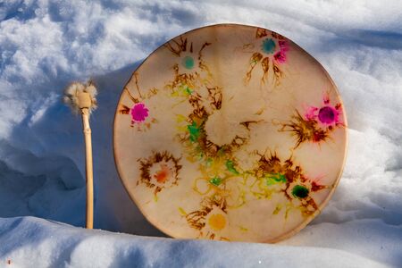 A close-up view of a vintage tribal sacred drum, shown outdoors in snow. Cultural instrument traditionally used in spiritual ceremonies.の写真素材