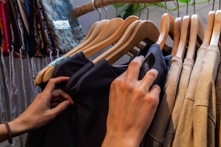 A close-up view on the hands of a young caucasian browsing rails in a small eco-friendly store. Locally handcrafted garments on wooden hangers.の写真素材