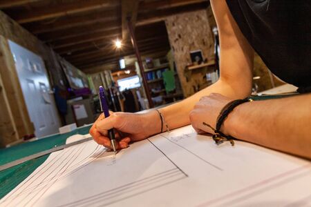 A closeup view on the arms of a clothing designer sketching ideas on a technical drawing table...
