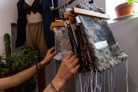 A young shopper browses small handmade tote bags inside a boutique store. Patterned reusable bags hang from a rustic rail in an environmentally friendly store.の写真素材