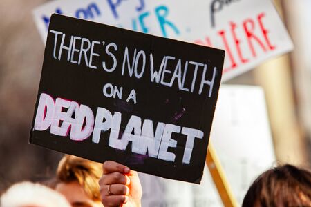 A closeup view of a homemade banner, reading there's no wealth on a dead planet, as a crowd of ecological protestors march on a city street.の写真素材