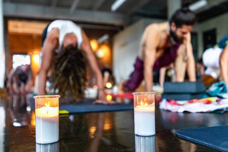Diverse group of people in yoga class. A closeup view of candles burning on the floor during a spiritual yogic lesson. Blurry people are seen in the background during 108 salutations to the sun.の写真素材