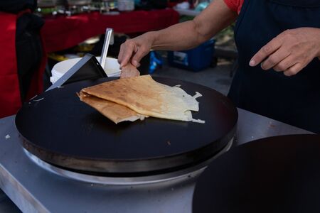 Fresh food at outdoor farmer's market. A closeup view on the hands of chef preparing pancakes at a stall during a local farmers market. Fast food sold outdoors with room for copy.の写真素材
