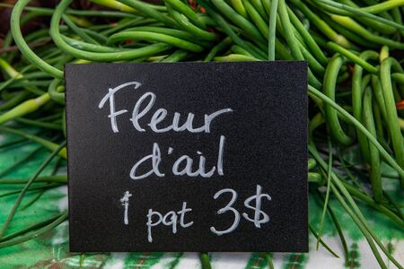 Organic produce at a farmer's market. A French Canadian price sign, saying garlic flowers (Allium...