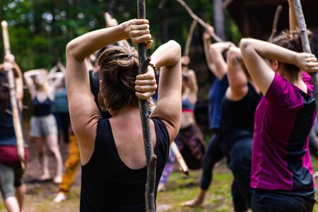 Diverse people enjoy spiritual gathering A close up view of a young caucasian woman holding a long stick behind her spine during a multicultural festival in natural surroundings.の写真素材