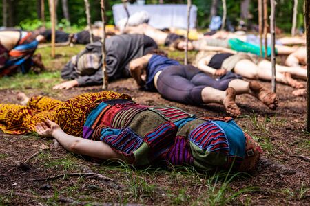 People having spiritual gathering. A colorful and intergenerational group of people are seen laying face down in a muddy woodland clearing as they practice meditation and relaxation.の写真素材