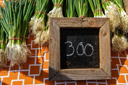Organic produce at a farmer's market. A three dollar price sign on a small chalkboard is seen up close on a traditional market stall selling fresh vegetables. Bundles of scallions are seen.の写真素材