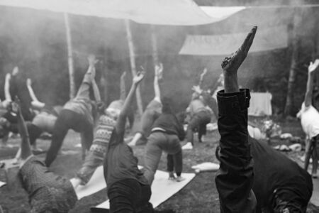 Diverse people enjoy spiritual gathering An atmospheric black and white view on a multiethnic group of mindful people practicing yoga poses in woodland during a shamanic retreat.の写真素材