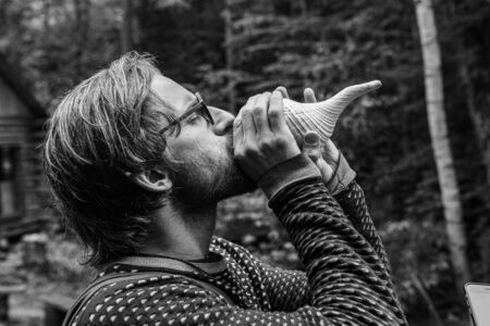 Diverse people enjoy spiritual gathering A monochrome view of a young shaman guy playing a sacred conch in woodland, a musical instrument made fro the shell of a sea snail.の写真素材