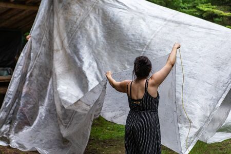 Diverse people enjoy spiritual gathering A young woman is viewed from behind, erecting a basic tent...