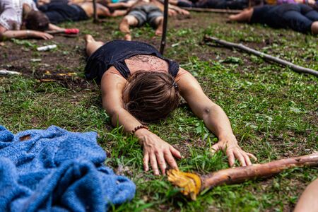 Diverse people enjoy spiritual gathering A close up and front view of a young woman lying face down on grass and earth during a celebration of multicultural meditation exercises in nature.の写真素材
