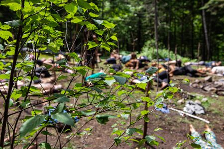 Diverse people enjoy spiritual gathering Blurry people are seen meditating behind tree branches...