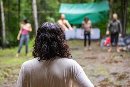 Diverse people enjoy spiritual gathering A woman with shoulder length black curly hair is viewed from behind as people gather in a circle at a campsite for mindful exercises, with copy space.の写真素材