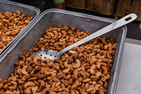 Organic produce at a farmer's market. Freshly roasted cashew nuts are view up-close, in a silver serving tray with metal spoon. Nutritional food sold by weight at an outdoor market, with copy-space.の写真素材