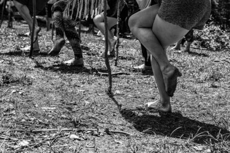 Diverse people enjoy spiritual gathering A closeup view on the legs of a group of people in standing yogic poses outdoors in nature, using sticks and bare feet close to earth.の写真素材