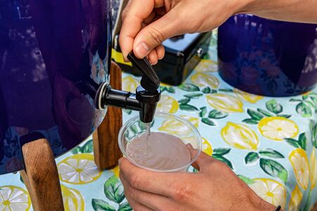 Fresh food at outdoor farmer's market. Hands of a man are seen close-up, using a drinks dispenser...