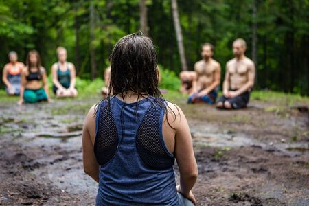Diverse people enjoy spiritual gathering A closeup and rear view of a woman with dark hair, kneeling on sacred ground in a forest clearing with a mixed group of people in deep meditation.の写真素材