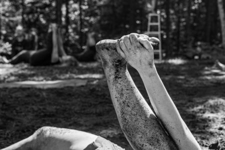 Diverse people enjoy spiritual gathering A close up and monochrome view on the dirty, mud splattered leg and arm of a person practicing yoga postures in woodland during retreat with room for copy.の写真素材