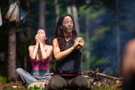 Diverse people enjoy spiritual gathering A young beautiful caucasian woman is seen covering her skin in sacred mud and clay during a shamanic ritual at a woodland retreat, with copy space.の写真素材