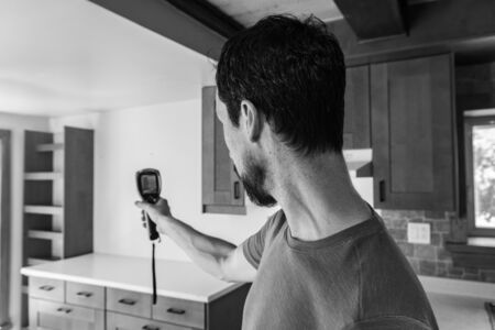 Indoor damp & air quality (IAQ) testing. A close up and monochrome view of a man using a small hand held thermal imagery device inside a family kitchen during a building survey, with copy-space.の写真素材