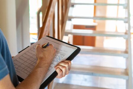 Indoor damp & air quality (IAQ) testing. A closeup view on the hands of a building inspector, filling in forms & paperwork, checking regulations are met inside a residential dwelling, with copy-space.の写真素材