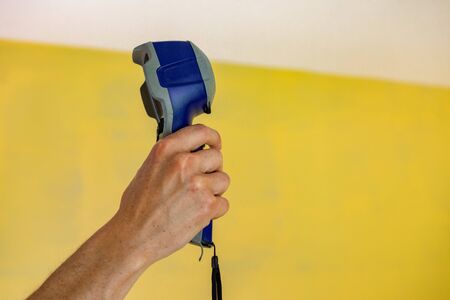 Indoor damp & air quality (IAQ) testing. A close up and side view of a man holding a handheld digital thermal imagery device, against a yellow wall during a residential property inspection.の写真素材