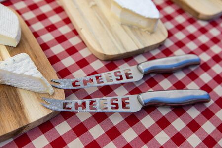 Fresh food at outdoor farmer's market. A close up view of traditional cheese boards and knifes, displayed on a red and white checked tablecloth on a market stall during a food fair.の写真素材