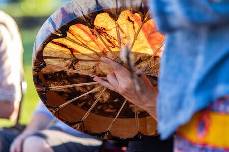 Sacred drums during spiritual singing. A close up view on the hands of a free spirited person holding a colorful and large native drum, using hand and fingers to grip the knot on the rear.の写真素材