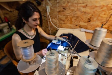 A side view of a young caucasian seamstress using an old-fashioned overlocking machine inside her...