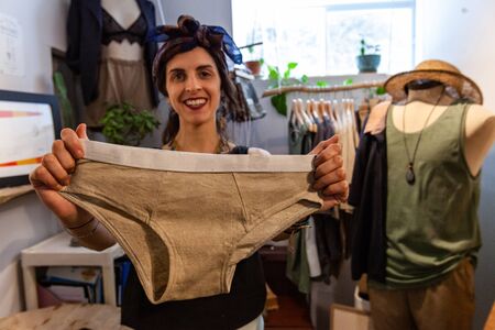 A young caucasian dressmaker looks happy as she shows eco-friendly beige colored underwear created by hand in design studio.の写真素材
