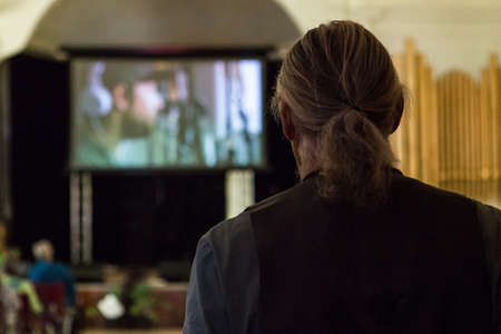 Pictured from the back with a blurry projection screen in the background