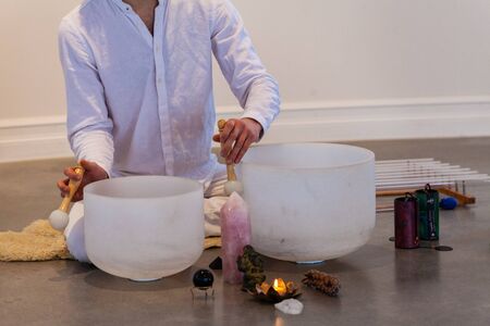 Man dressed in white, sitting on a sheep skin with a close up on his hands playing crystal bowls...