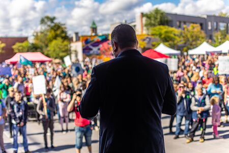 Selective focus of man on stage from the back taking to crowd. Group of people at open public space...