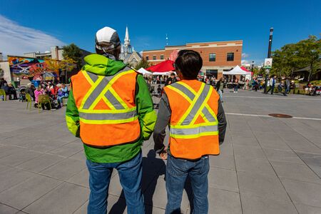 Two men from the back with high emergency clothing at public space protecting and looking out at...