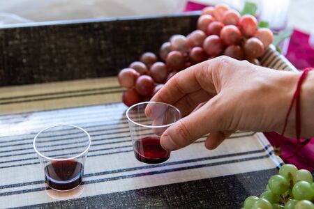 Close up of hand grabbing wine cup for tasting. Detail of oenology experience. Decorated with grapes and dainty tableclothの写真素材