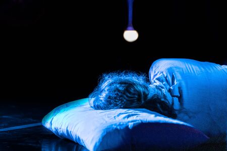 Close up photo of male or female actor lying on a pillow on stage in the spotlights performing in a drama play in a theaterの写真素材