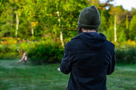 Backside view photo of a person standing in a grass field in nature while looking at somebody who seems to practice yogaの写真素材