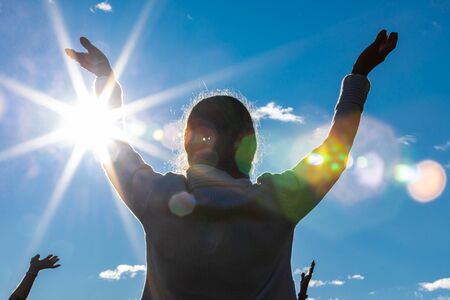 Backside and low angle view photo of person spreading arms to the sky in a participation of yoga session in nature settingの写真素材