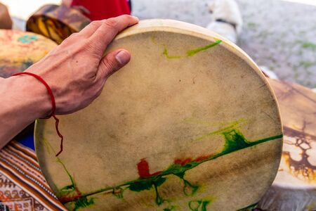 close up on caucasian mans hand holding sacred drum, new colourful native american leather drum During the outdoor exhibitionの写真素材