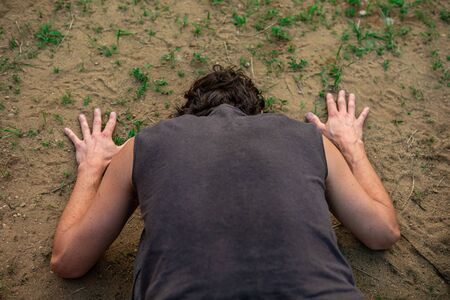 close up and high angle view of a man in a kneeling and bent forward facing pose, facing The soil of...