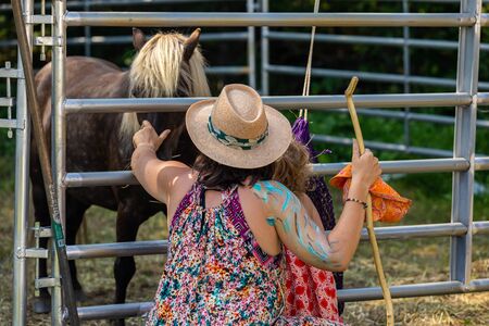 close up and back view of woman and his child playing with a beautiful brown horse behind the barrierの写真素材