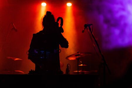 Fusion of culture and modern music event. silhouette of a DJ during a musical performance at night, as he holding headphone and using electronic music equipmentの写真素材